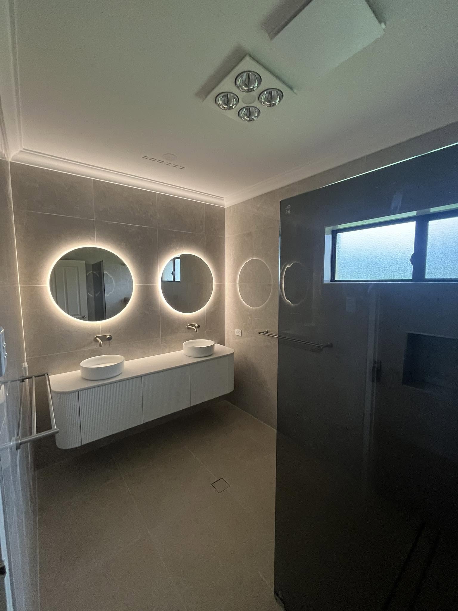 Completed bathroom renovation with double vanity and backlit mirrors